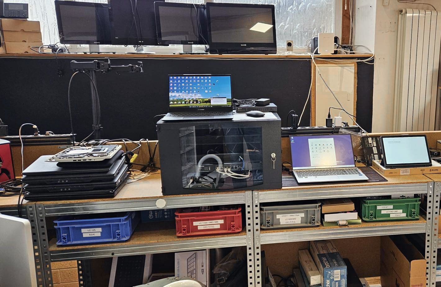 Étagères de l’atelier avec des ordinateurs portables, des tablettes et une petite baie réseau.