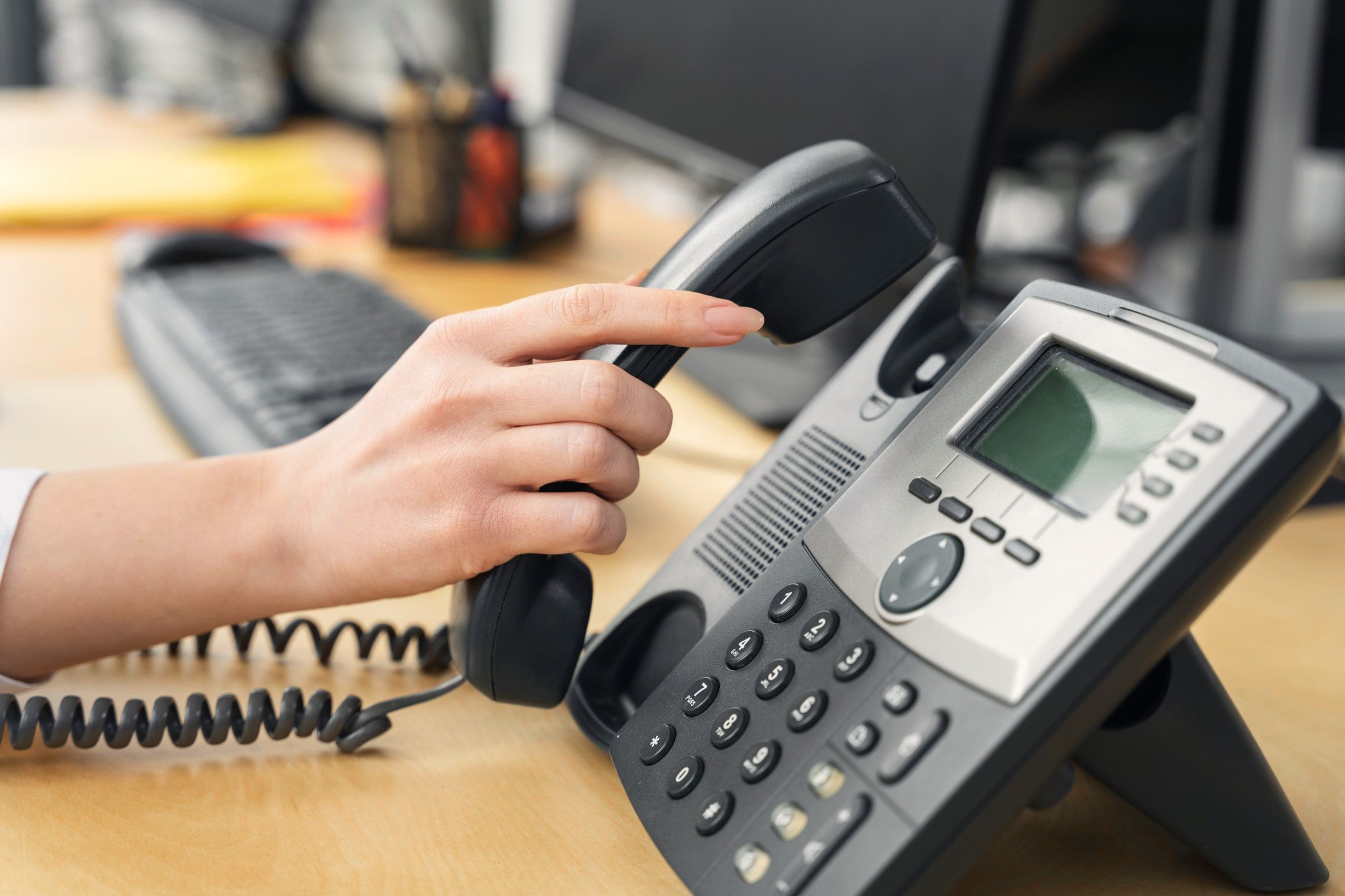 Une main décroche le combiné d’un téléphone de bureau IP.